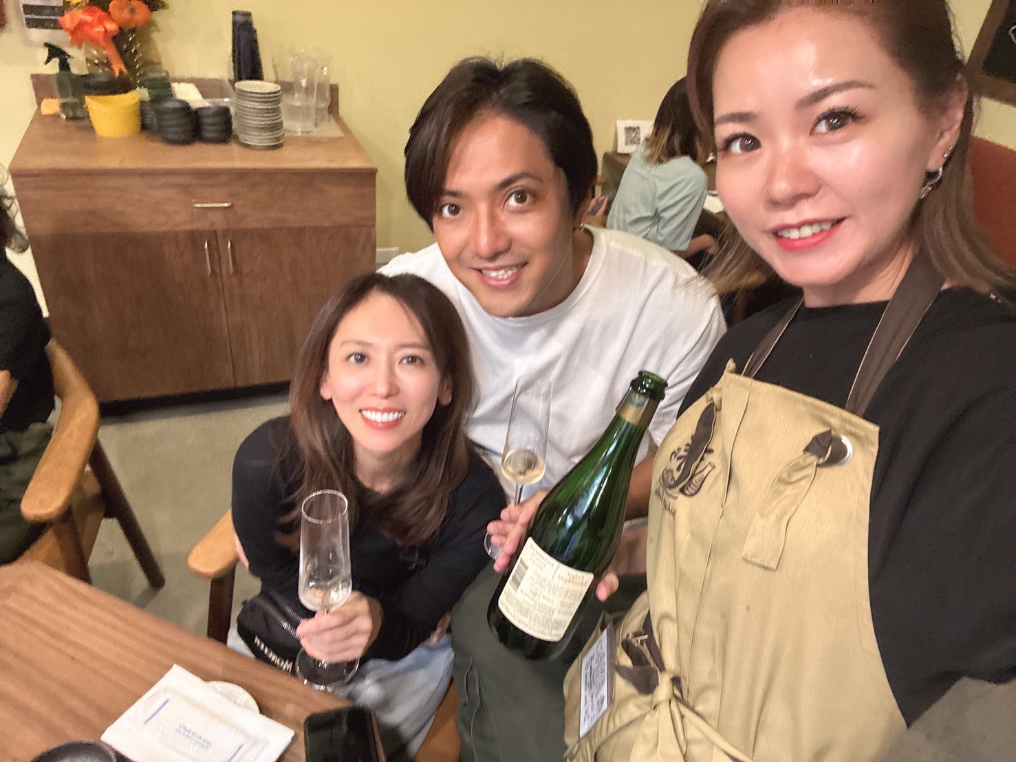 Three people smiling together at LaLa, with a bottle and glasses.